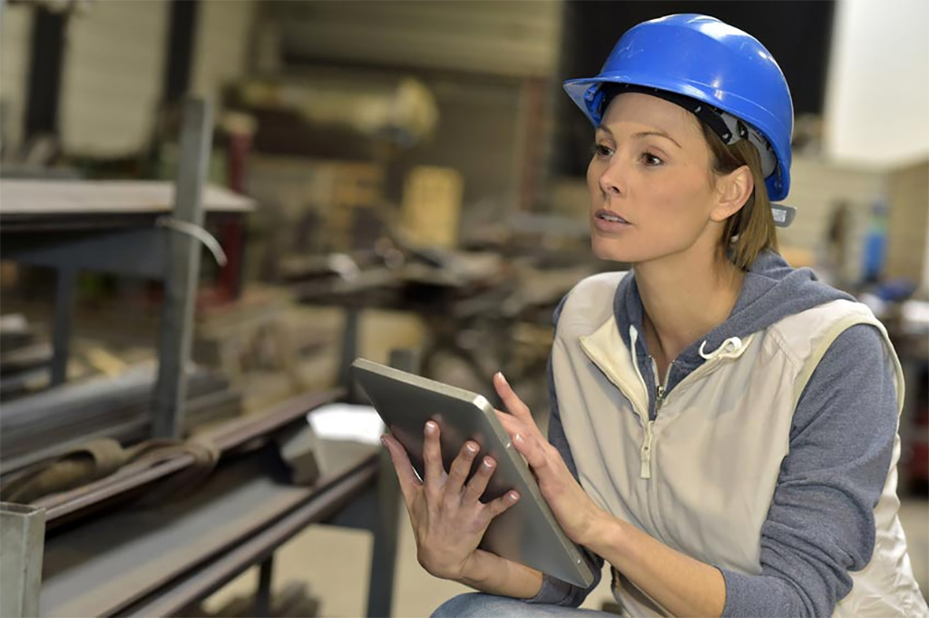 Una mujer con casco azul maneja una tableta en el interior de una fábrica.