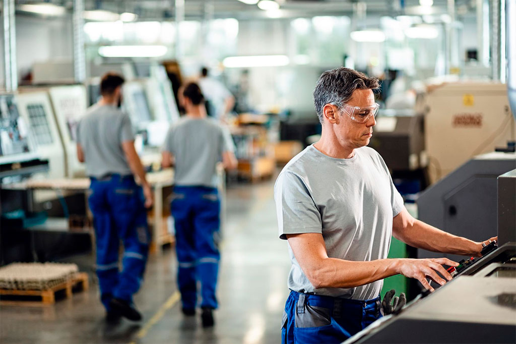 Trabajador adulto medio que opera una máquina cnc mientras trabaja en una instalación industrial