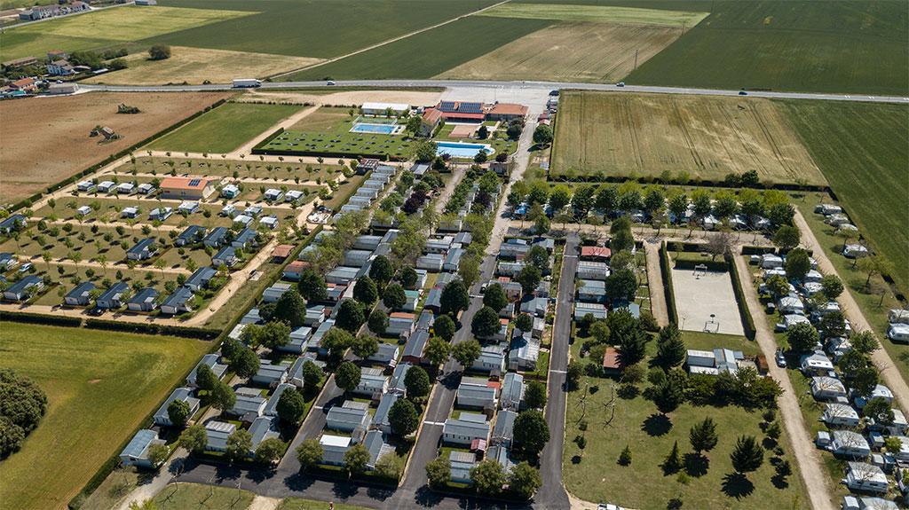 Vista aérea de un camping. Se ven tres filas de bungalows y dos piscinas rodeadas de hierba al fondo.