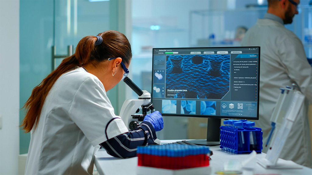 Científico de biotecnología investigando en laboratorio usando microscopio y escribiendo en ordenador