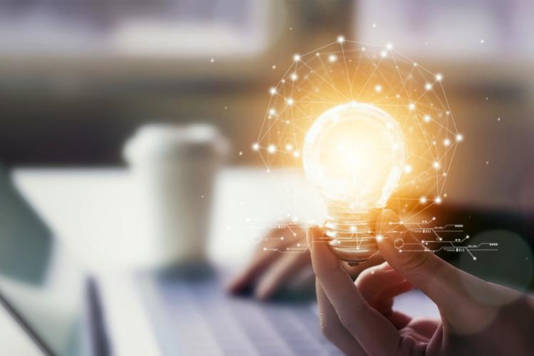 Mano sujetando bombilla sobre ordenador portátil