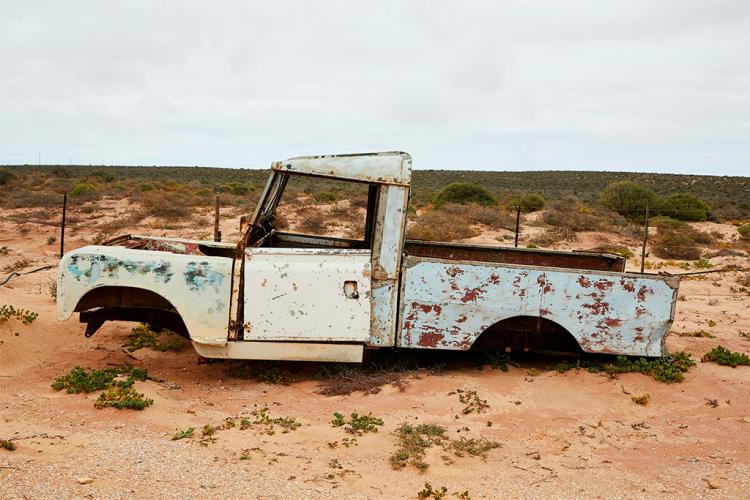 Imagen de una pick-up blanca en terreno árido. El vehículo tiene claros signos de deterioro, entre ellos, no tener ruedas y tener muchas manchas de óxido.
