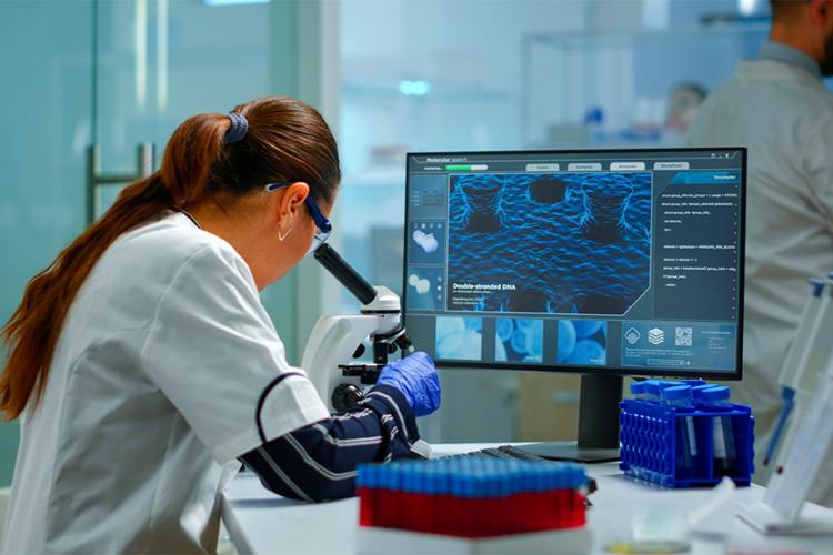 Científico de biotecnología investigando en laboratorio usando microscopio y escribiendo en ordenador