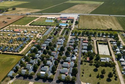 Vista aérea de un camping. Se ven tres filas de bungalows y dos piscinas rodeadas de hierba al fondo.